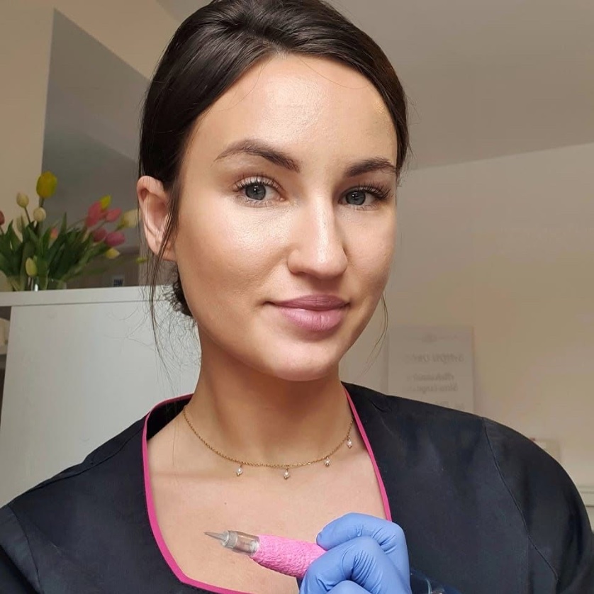 Aleksandra Stawiszyńska w czarnym fartuchu z różową lamówką, z różowym dermografem w dłoni w rękawiczce